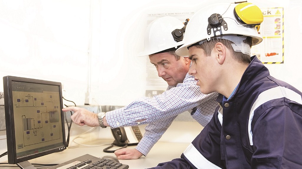 Two men looking at a computer screen wearing hard hats.